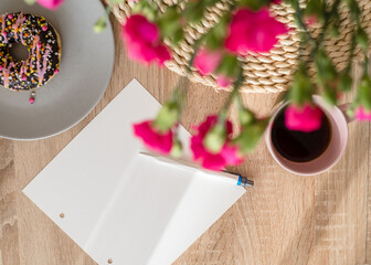 Cozy breakfast and planning. Notepad and pen, cup of coffee, pink donut, flowers and candles on the table. Women's desktop. Top view