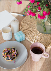 Cozy breakfast. Cup of coffee, pink donut, candles and flowers on the table. Weekend breakfast, relax, girls time