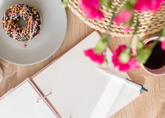 Cozy breakfast and planning. Notepad and pen, cup of coffee, pink donut, flowers and candles on the table. Women's desktop. Top view