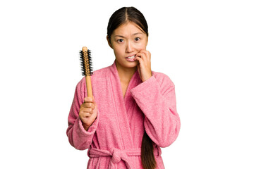 Young asian woman holding an hair comb isolated biting fingernails, nervous and very anxious.