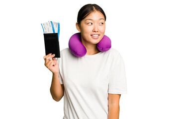 Young asian woman with inflatable travel pillow on her neck holding passport isolated looks aside smiling, cheerful and pleasant.