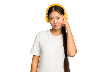 Young asian woman listening to music with headphones isolated pointing temple with finger, thinking, focused on a task.
