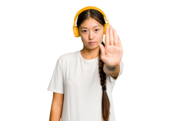 Young asian woman listening to music with headphones isolated standing with outstretched hand showing stop sign, preventing you.