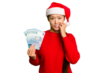 Young asian woman celebrating Christmas holding banknotes isolated biting fingernails, nervous and very anxious.