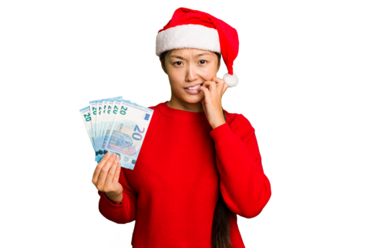 Young asian woman celebrating Christmas holding banknotes isolated biting fingernails, nervous and very anxious.