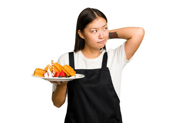 Young asian waitress woman holding waffles isolated touching back of head, thinking and making a...