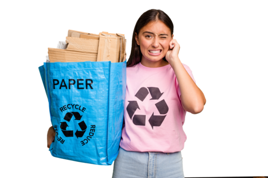 Young caucasian woman holding a recycling bag full of paper to recycle isolated covering ears with hands.