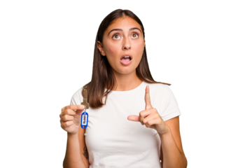 Young caucasian woman holding a home keys isolated pointing upside with opened mouth.