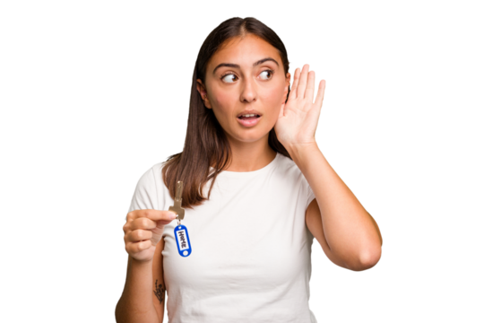 Young caucasian woman holding a home keys isolated trying to listening a gossip.
