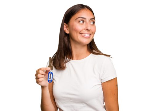 Young caucasian woman holding a home keys isolated looks aside smiling, cheerful and pleasant.