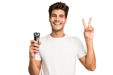 Young caucasian man holding a razor isolated joyful and carefree showing a peace symbol with fingers.