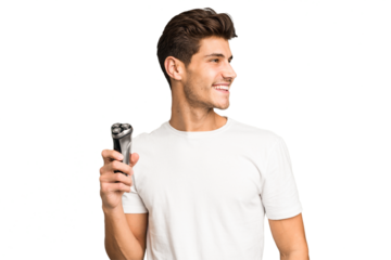 Young caucasian man holding a razor isolated looks aside smiling, cheerful and pleasant.