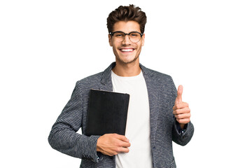 Young teacher caucasian man holding a book isolated smiling and raising thumb up