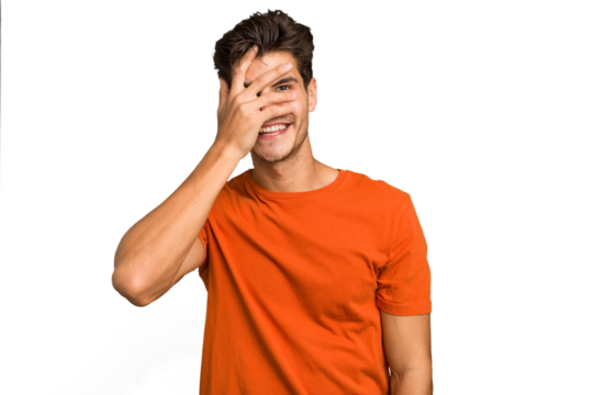 Young caucasian handsome man isolated blink at the camera through fingers, embarrassed covering face.