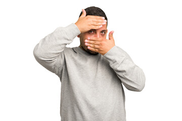 Young caucasian man isolated blink at the camera through fingers, embarrassed covering face.