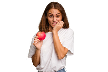 Young caucasian woman holding a red apple isolated biting fingernails, nervous and very anxious.