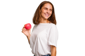 Young caucasian woman holding a red apple isolated looks aside smiling, cheerful and pleasant.
