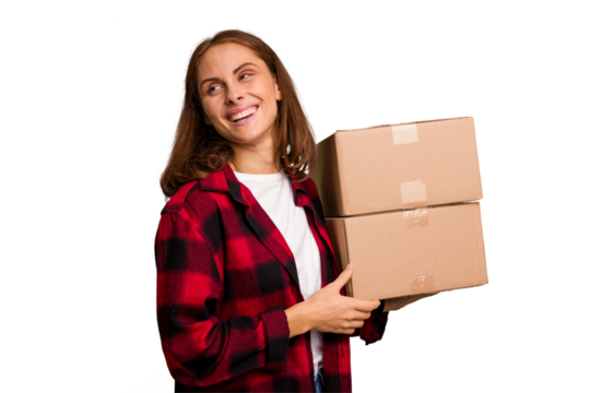 Young caucasian woman moving while picking up a box full of things isolated looks aside smiling, cheerful and pleasant.