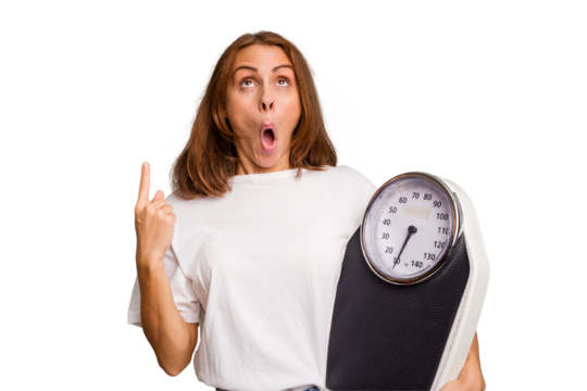 Young caucasian woman holding a scale and measure tape isolated pointing upside with opened mouth.