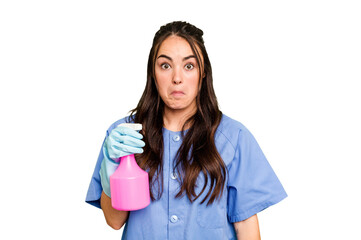 Young cleaner caucasian woman isolated on green chroma background shrugs shoulders and open eyes confused.