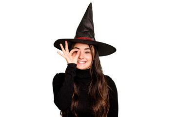 Fototapeta premium Young caucasian woman dressed as a witch isolated on green chroma background excited keeping ok gesture on eye.