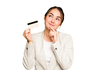 Young caucasian woman holding a credit card isolated on green chroma background looking sideways...