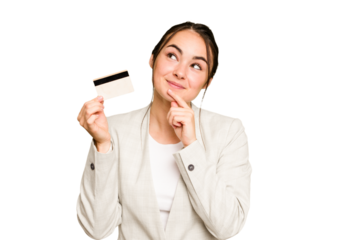 Young caucasian woman holding a credit card isolated on green chroma background looking sideways with doubtful and skeptical expression.