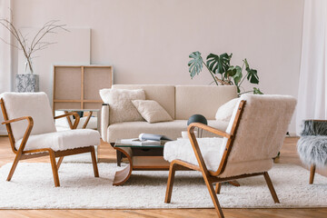 Stylish interior of living room with white cozy armchairs, sofa, coffee table, canvases, plants. Aesthetic Scandinavian home interior design.