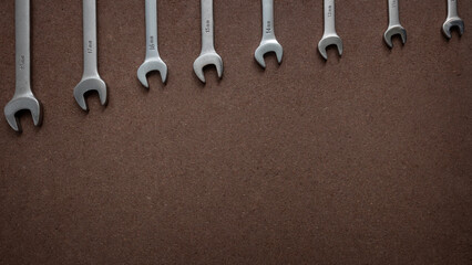 Spanners with different sizes on a wooden board. Top down view flat lay with workshop tools on a brown OSB board. Wooden background with wrenches lined up according to size and empty space for text