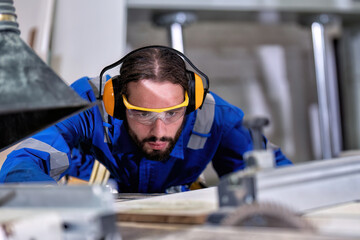 In wooden industrial carpenter man wearing ear muff and safety glass working on circular saw machine