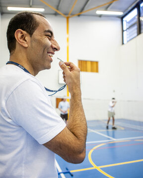 Sports Students: PE Teacher. A smiling gym instructor refereeing a game of badminton. From a series of related images.