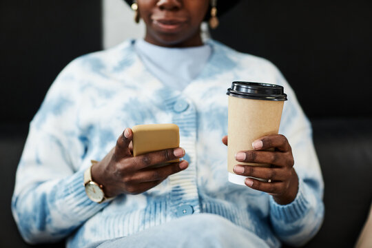 Close up of young black woman using smartphone and holding coffee cup, gen Z communication concept