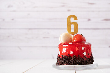 The number Six on a red birthday cake on a light background