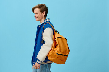 student with a backpack on his shoulder posing on a blue background