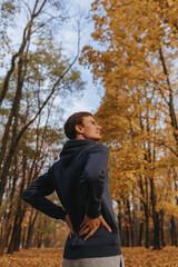 Low angle of sportsman exercising and stretching back while training on sunny day in autumn park 