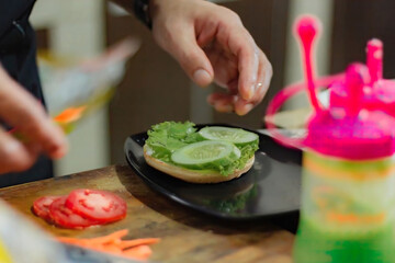 Chef puts tomato slice for burger filling, on kitchen utensils background.