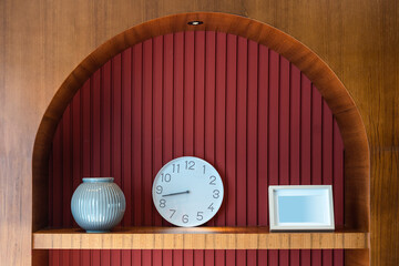 Modern clock, white photo frame, blue ceramic vase on the wooden shelf built-in of the red wall...