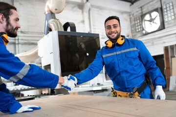 Arab carpenter in safety uniform check hand with caucasian friend at wood factory