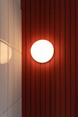 Beautiful modern round shape wall lamp light bulb decoration for home and living on the red and white wall background with copy space for text.