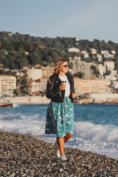 Young beautiful girl with coffee on an autumn sunny day walks on the beach of the Mediterranean Sea