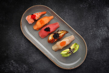 Assorted Nigiri sushi on a plate, on dark concrete