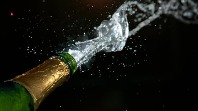 Super slow motion of Champagne explosion with flying cork closure, black background, opening champagne bottle closeup.