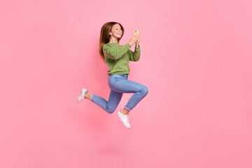 Full length photo of cheerful sweet schoolgirl wear green sweatshirt jumping high chatting modern device isolated pink color background