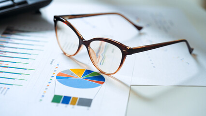 The glasses on the business office desk at the end of the work schedule. Financial spreadshets and reports with data for analysis. Set of documents and glasses set various items on office desk.