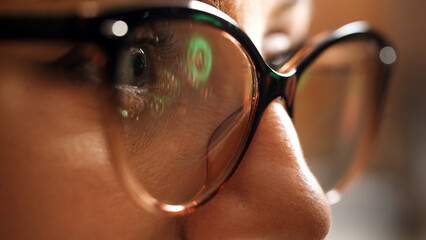 Woman in glasses looking on the monitor and surfing Internet. The monitor screen is reflected in the glasses. Work at night. Home Office. Remote work