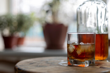 Glass of whiskey on ice with bottle on wooden bar