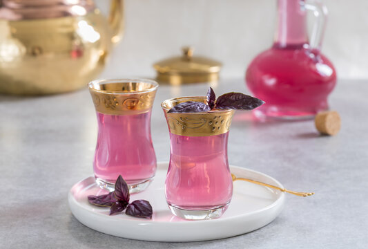 Pink basil Sherbet or Sharbat drink in two armudu glasses with copper teapot and glass cruet on background. Selective focus, horizontal, light background