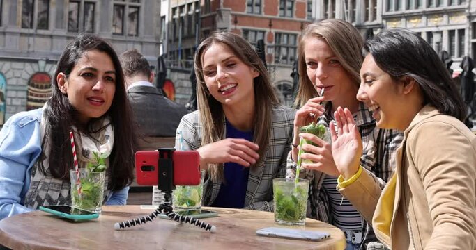 Antwerp, Belgium, May 21, 2021, Four multi ethnic female friends, tourists or students sitting at a cafe terrace in the city center using mobile phone for a video call. High quality FullHD footage