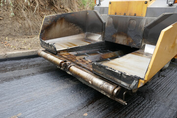 A paving machine placing fresh asphalt or bitumen on a gravel base during construction