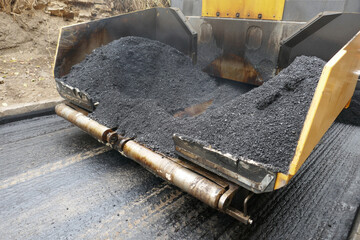 A paving machine placing fresh asphalt or bitumen on a gravel base during construction